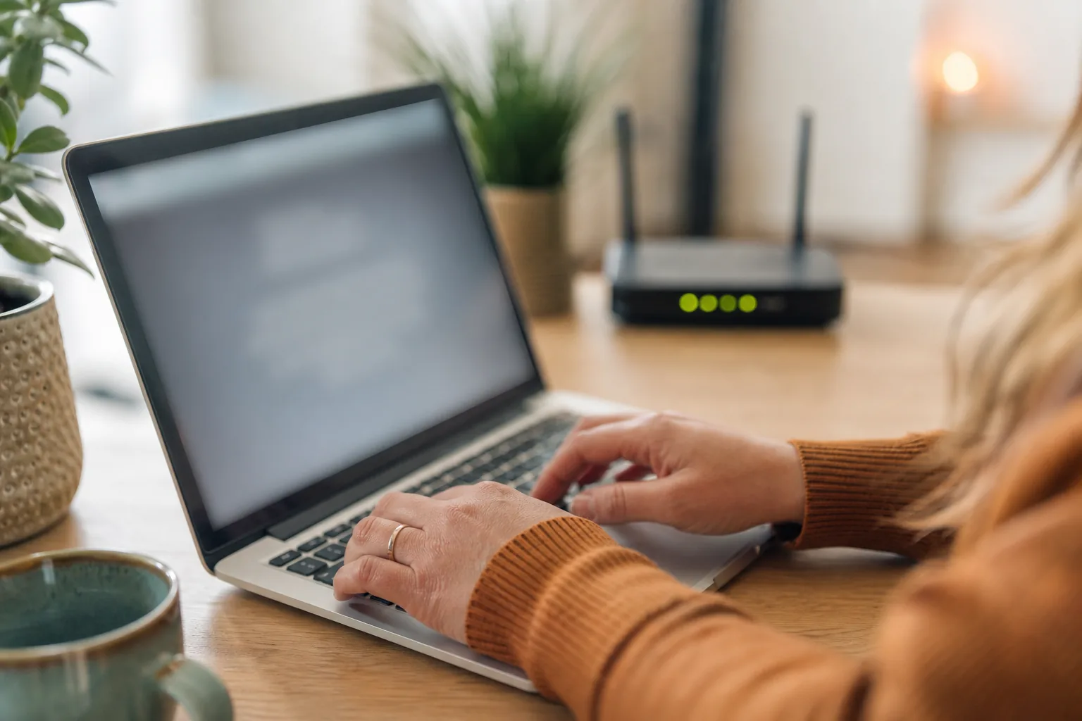 Vrouw aan een thuiswerkplek kijkt aandachtig naar een inlogpagina op haar laptop, naast haar een router met brandende lampjes op het bureau